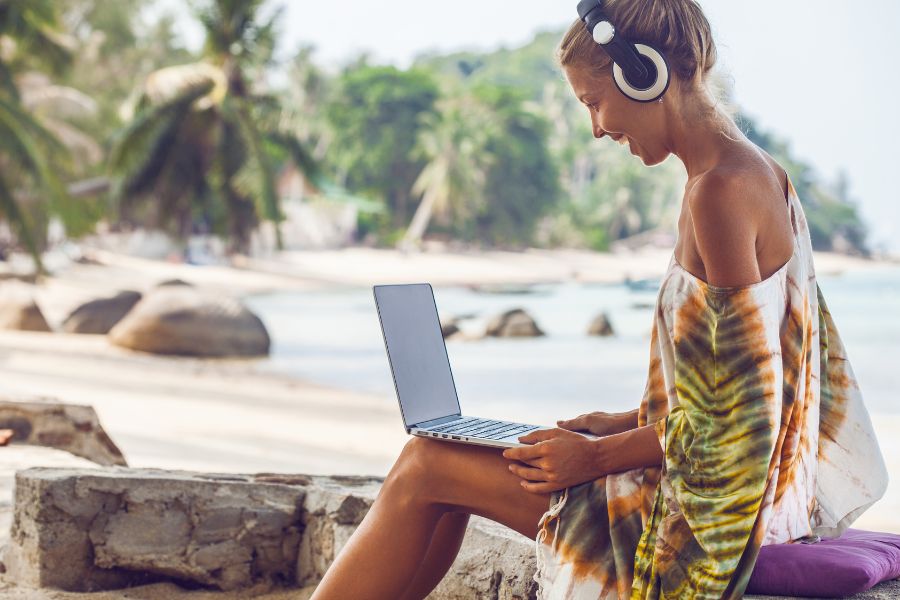 Woman working on beach with laptop and headphones
